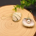 Elegantes pendientes de perlas con forma de concha dorada en un soporte de madera - Pendientes de Perlas de Concha Natural