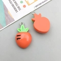 Detailed view of two resin carrot pendants with green leaves and metal rings on light background - Orange Resin Carrot / 14*23mm