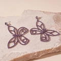 Detailed close-up of butterfly earrings with purple zircons on a beige stone surface - Purple