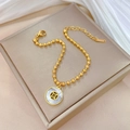 Golden beaded stainless steel bracelet with white shell pendant on jewelry box - Gold
