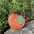 Close-up of orange peach-shaped kid's crossbody bag with litchi grain texture on a rock - Round Radish Red Orange