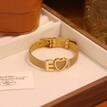 Détail d'un bracelet en maille dorée avec breloques cœur et lettre E sur un coffret en bois - Lettre E
