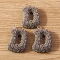 Macro shot of three taupe letter D pendants with rose textures and silver hooks on wood - Letter D / Khaki