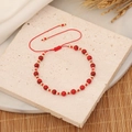 Handmade woven bracelet with red stone beads and gold metal spacers on light stone background - Red
