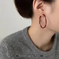 Detail view of 4.5cm red wavy twisted hoop earring on model with grey knitwear - Red Twisted Large