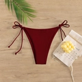 Detail of burgundy bikini bottom with side ties on a wooden table with palm leaf - Burgundy