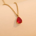 Golden necklace with a red teardrop-shaped gemstone pendant on beige surface - June (Red)