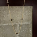 Detail of gold necklace featuring five black clover motifs on vintage glass background - Clover Necklace / Gold Black