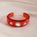 Macro-opname van een rode hars armband met strass-steentjes op beige zijden weefsel - Rood - Transparant