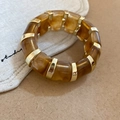 Dettaglio del bracciale a maglie in acrilico ambra e metallo dorato su lino beige - Marrone Ambra