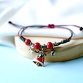 Detail of red and green braided Christmas bracelet with star and bell charms on wood - Bell