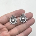 Nahaufnahme von silbernen Vintage-Flammenherz-Anhängern in der Hand zur Größendarstellung - Altsilber Metall Heiliges Herz