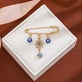 Macro detail of gold evil eye brooch with nautical helm and blue teardrop pendant in gift box - Helm Evil Eye Style (Z338-3)