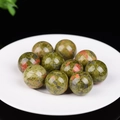 Polished green and red cat eye stone spheres arranged on a white decorative plate - Unakite