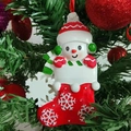 Close-up of resin snowman in Christmas stocking ornament hanging on a festive tree branch - Red