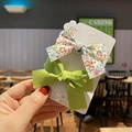 Close-up of green solid and floral bow hair clips held by hand on display card - 1# Floral Green Set of 2