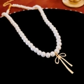 Close-up of pearl choker necklace with gold bow pendant on black velvet display - White Pearl Bowknot Necklace