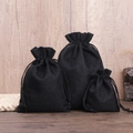 Three sizes of black drawstring linen jewelry bags displayed on a wooden background - Black