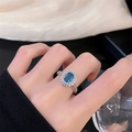 Macro detail of oval blue topaz ring with halo crystal accents on a silver band - Adjustable Open / Blue Gemstone Pave Style (JZ4471)