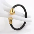 Detail of twisted cable cuff bracelet featuring black texture and golden fist pendants - Black & Gold