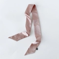 Detail eines rosa Satin-Seidenschals mit silbernen Ziernieten und schwarzem Etikett auf Weiß - Altrosa