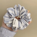 Blau-weiß gestreifter Stoff-Scrunchie mit handgefertigtem Etikett in der Hand - Hellblau Zebrastreifen