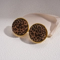 Detalle macro de pendientes redondos con estampado de leopardo y borde de metal dorado - Poste de plata para pendientes - Café