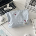 Dettaglio flat lay della trousse a righe blu con ricamo a fiocco rosso su scrivania bianca - Striscia Blu Fiocco Rosso