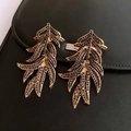 Nahaufnahme goldener Blatt-Quasten-Ohrringe mit dunklen Pavé-Kristallen auf schwarzem Leder - Silberstecker - Gold - Schwarz