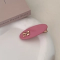 Detail of pink oval hair clip with gold bow accent on aesthetic book background - Pink