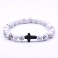 Detailed macro view of white turquoise beads with a black cross charm on a stretch bracelet - White