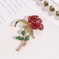Dettaglio spilla a rosa in smalto rosso con strass verdi e stelo dorato su un libro - Stile Rosa Rossa