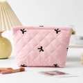 Detailed close-up of pink quilted cosmetic bag with black embroidered bow details - Pink