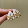 Nahaufnahme eleganter Seestern- und Muschelohrringe in Gold- und Weißoptik für den Urlaub. - Stil mit Silber-Ohrstecker / Gold-Weiß