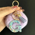 Détail d'un porte-clés pompon violet avec lettre G en résine et paillettes en cœur - Lettre G