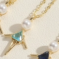 Detalle del colgante de niña en metal dorado con perla y piedras de circón azul brillante - Circonita Azul