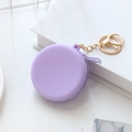 Round purple silicone coin purse with golden keychain on white book background - Purple