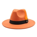 Détail d'un chapeau en laine orange avec ruban noir, badge M doré et décoration plume - Orange