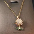Golden sunflower pendant necklace with clear crystals and green gems on a brown board - Gold - Rotating Sunflower Green Leaf