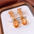 Macro shot of vintage amber water-drop pendant earrings with golden crystal floral details - Amber Gold (Silver Pin)