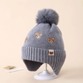 Detail of grey winter knit hat for kids featuring bear embroidery and a fluffy pompom - 3-8 Years / Gray