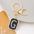 Detailed close-up of a golden G-letter keychain with black enamel and sparkling rhinestones - Letter G