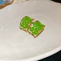 Macro shot of gold-plated C-shaped flower earrings with green enamel petals on white tray - Silver Needle - Green Flower