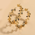 Dettaglio macro di orecchini a foglia placcati oro 14K con cristalli blu e motivi a vite - Foglia in Zirconia Blu Zaffiro