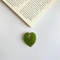 Green heart-shaped acrylic leaf phone grip with natural vein texture on book background - Philodendron Melanochrysum (m143)