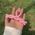 Pinza de pelo retorcida rosa mate sostenida sobre un fondo de hierba verde - Rosa