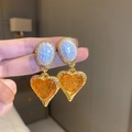 Vintage style gold earrings featuring amber resin heart pendants held on fingers - Oval Heart Stud / Amber White