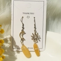 Macro detail of sun and moon stainless steel earrings with handmade wire-wrapped yellow stones - Topaz
