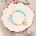 Detail eines Heishi-Armbands mit rosa Herzanhänger und Strass in einer weißen Schale - 4# Seeblau
