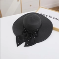 Detail of wide brim black straw hat with large bow and white pearls on white table - M / Black